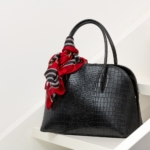 Schwarze Handtasche mit rotem Tuch auf weißem Regal