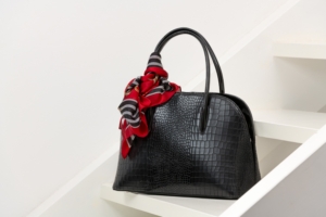 Schwarze Handtasche mit rotem Tuch auf weißem Regal