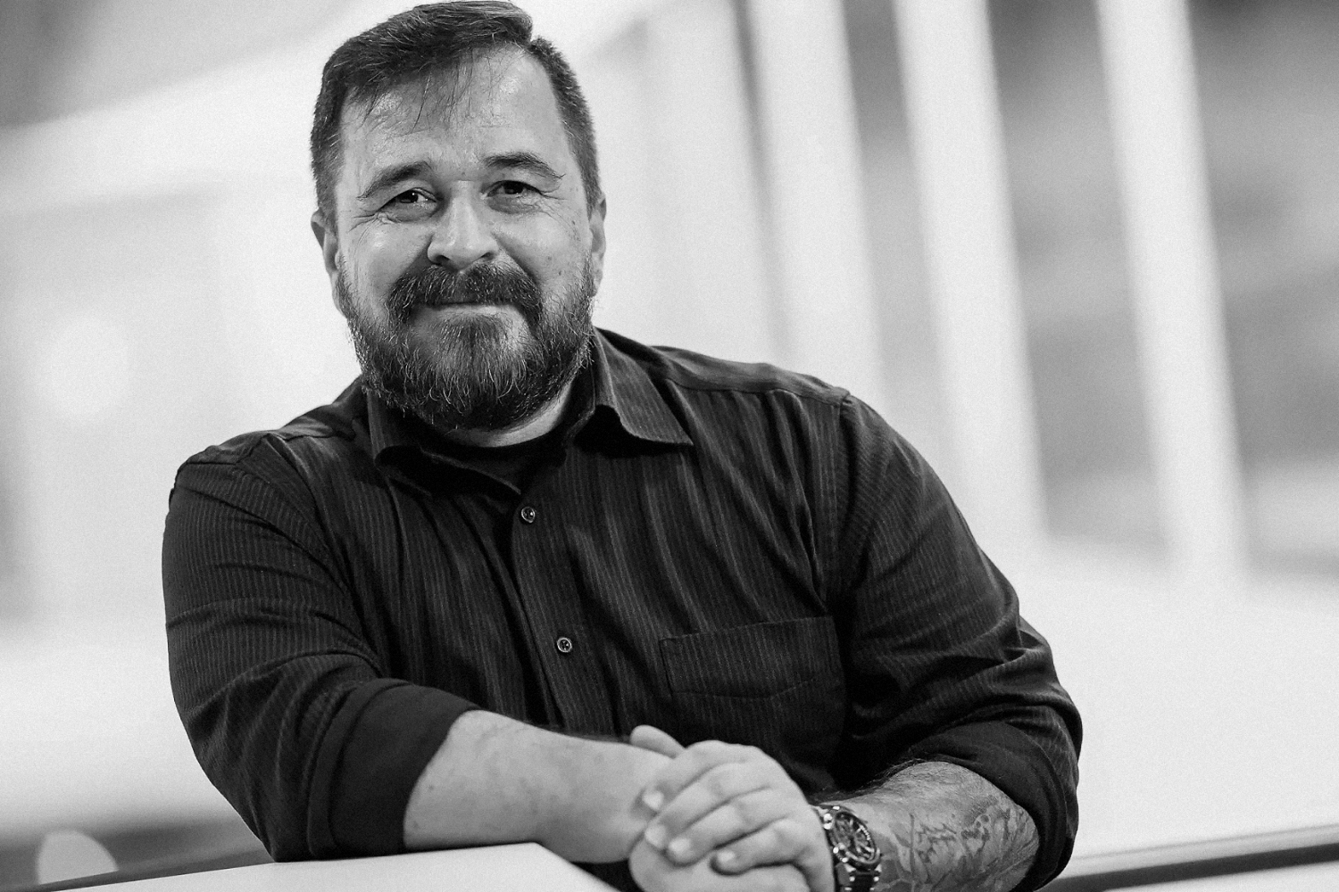 ulrich-roth-businessfotografie_WSP_ Businessfotograf Ulrich Roth lächelt in die Kamera, schwarz-weißes Porträt mit verschränkten Armen vor neutralem Hintergrund