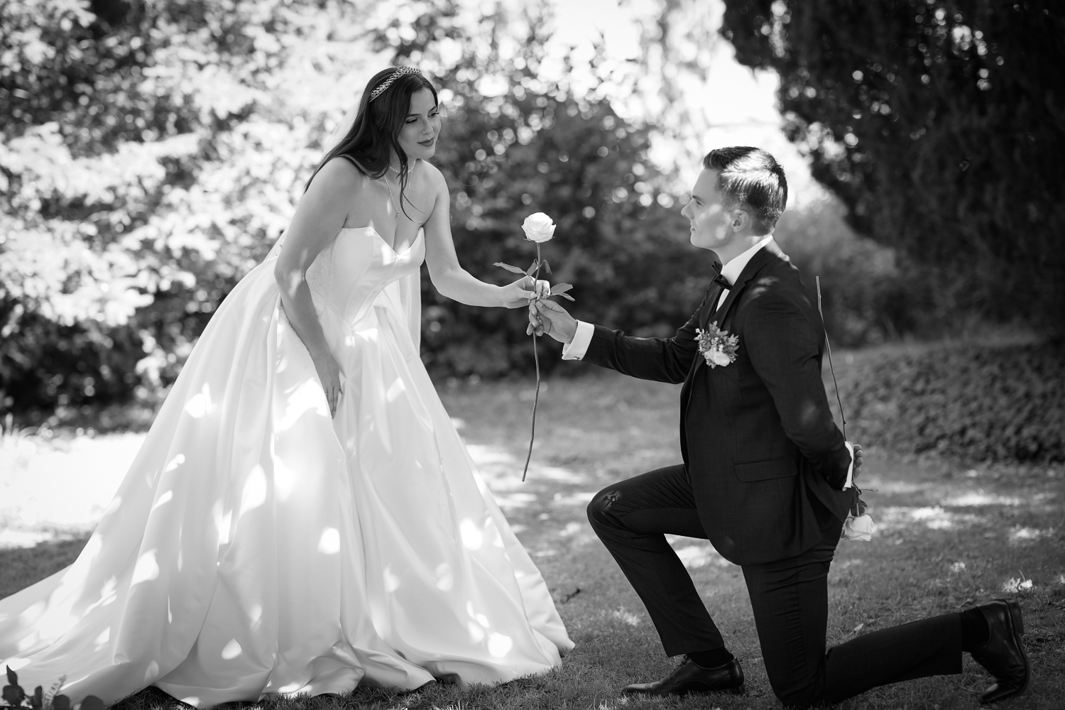 Bräutigam kniet und überreicht der Braut eine Rose während eines romantischen Moments bei der Sommerhochzeit im Schloss Edesheim am 08.08.2025