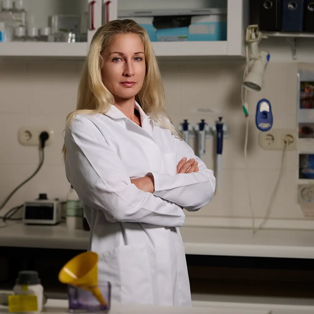 Porträt einer Wissenschaftlerin im weißen Laborkittel mit verschränkten Armen in einem modernen Labor, fotografiert von Ulrich Roth