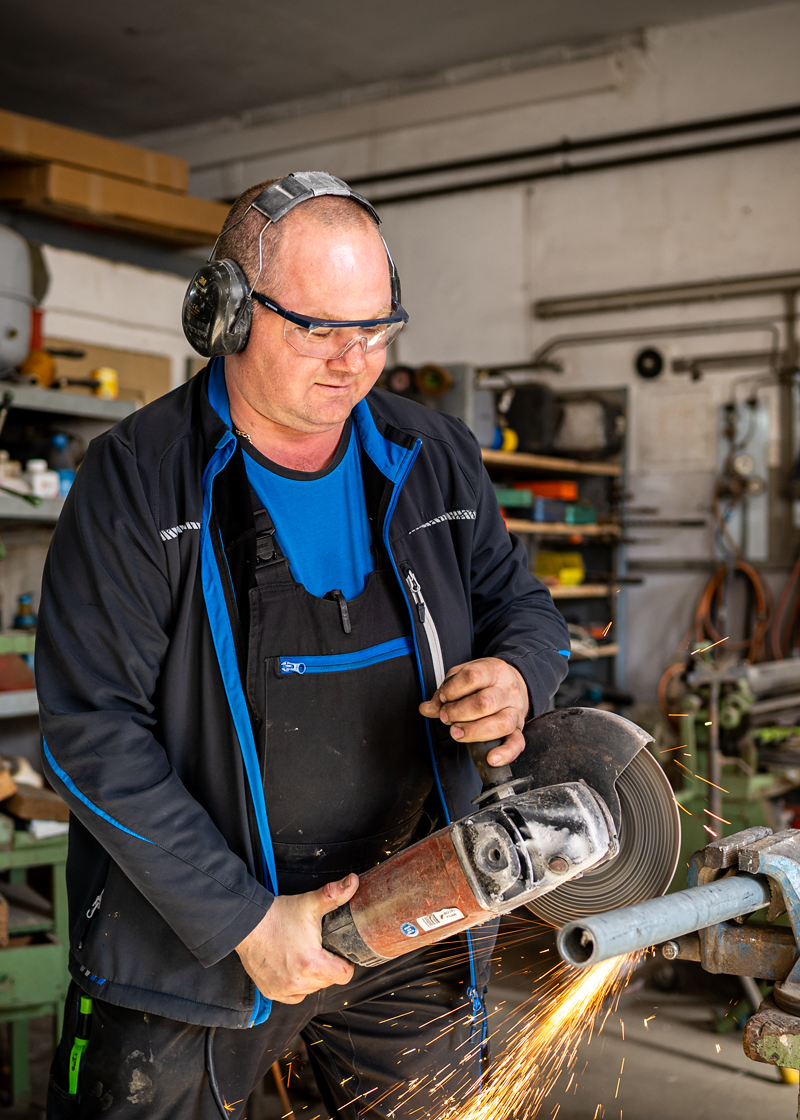Mitarbeiter mit Schutzbrille und Gehörschutz beim Trennen eines Metallrohrs in einer Werkstatt