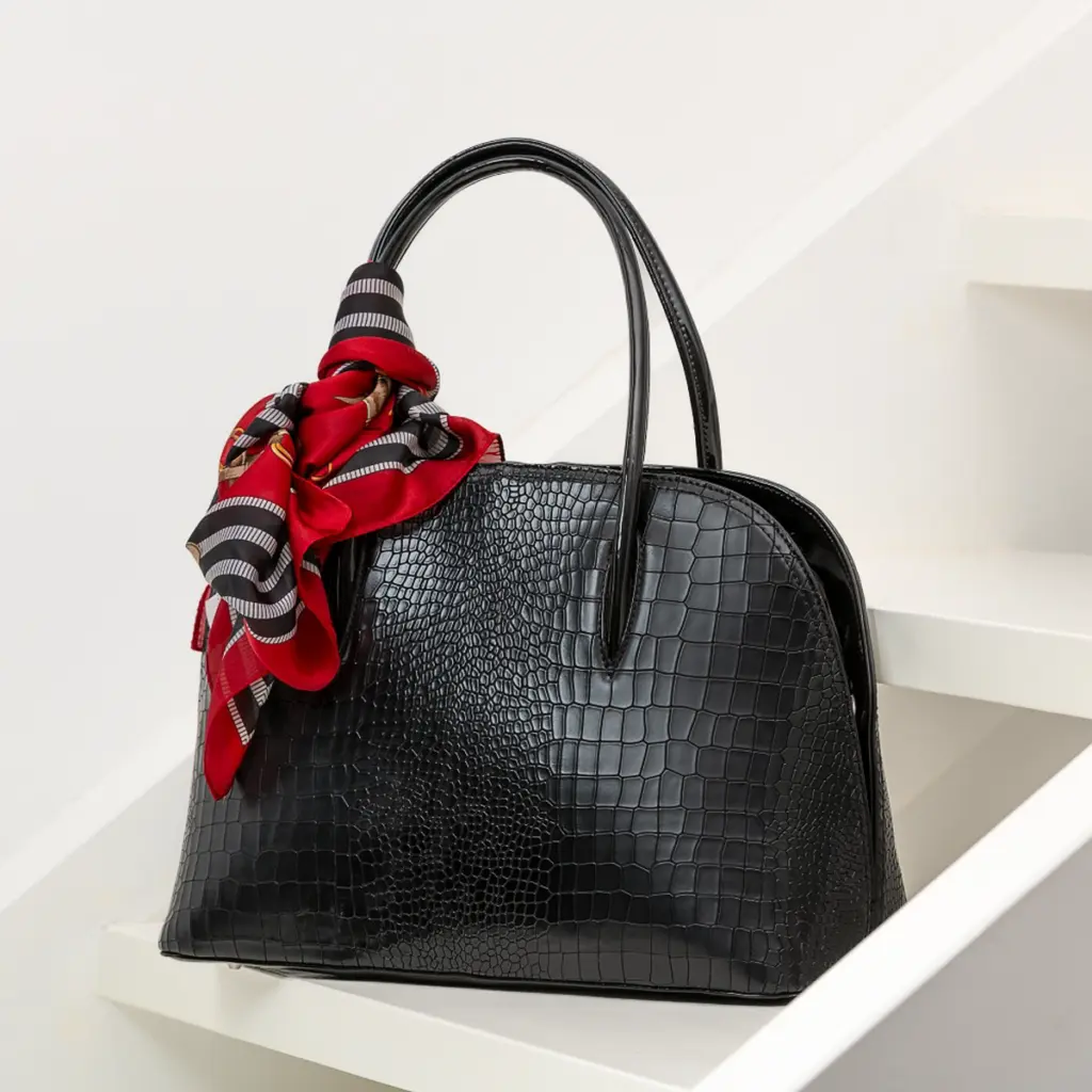 Produktfoto einer schwarzen Lederhandtasche mit rotem Seidentuch als Accessoire, fotografiert von Ulrich Roth