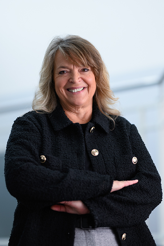 Businessporträt einer lächelnden Frau mit verschränkten Armen vor hellem Hintergrund.