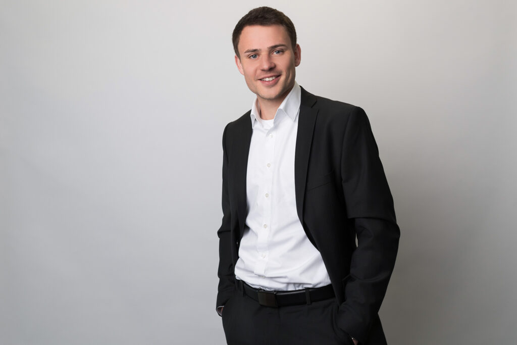 Businessporträt eines Mitarbeiters im Anzug vor neutralem grauem Hintergrund