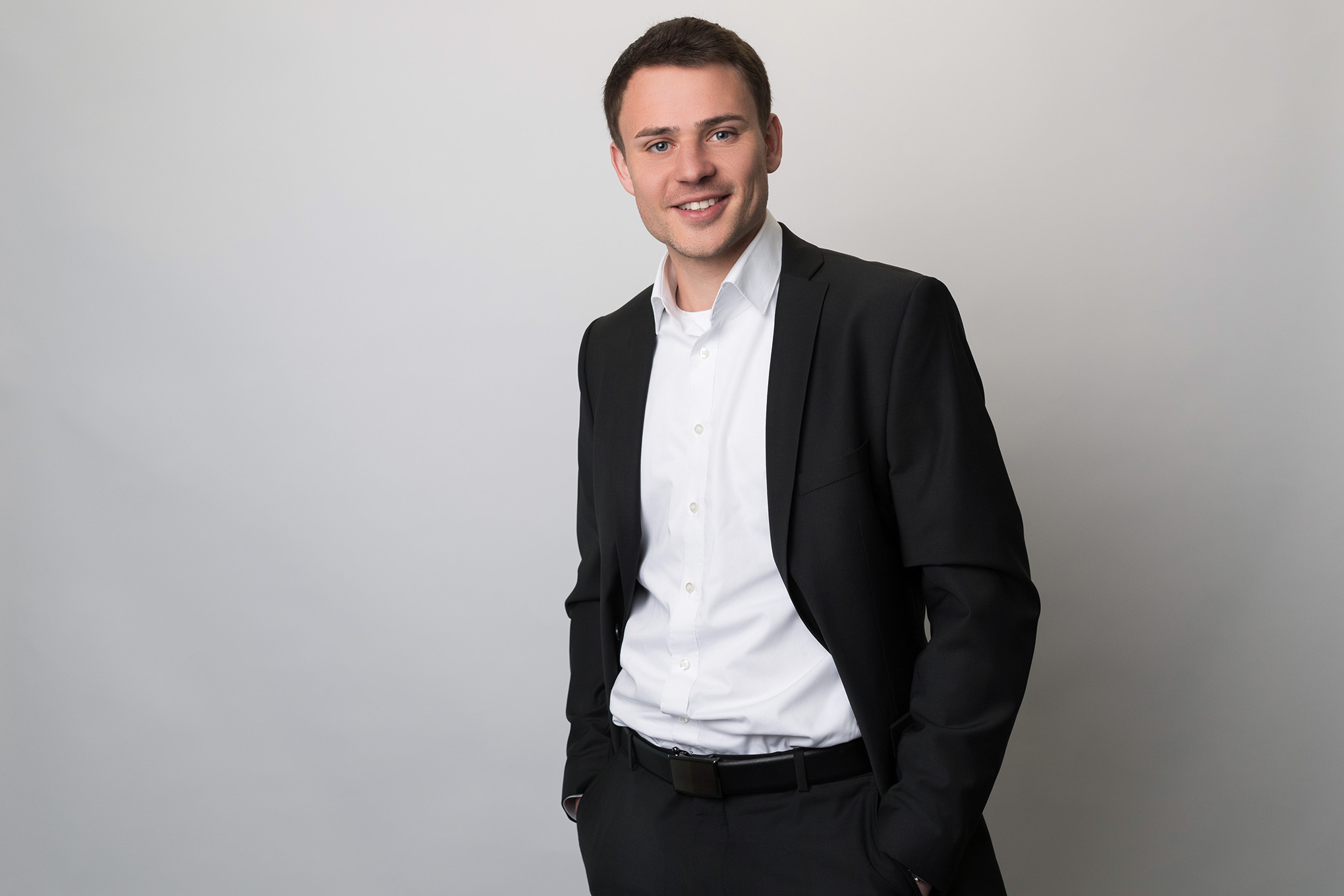 Businessporträt eines Mitarbeiters im Anzug vor neutralem grauem Hintergrund