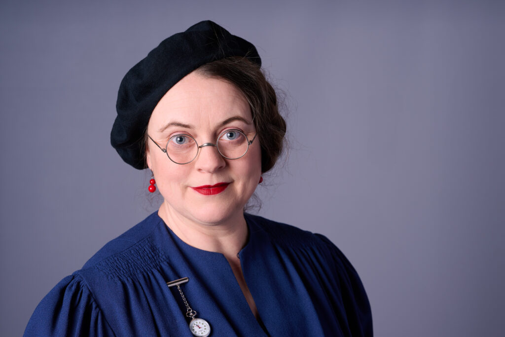 Professioneller Corporate Headshot einer Frau mit Brille und rotem Lippenstift vor grauem Hintergrund