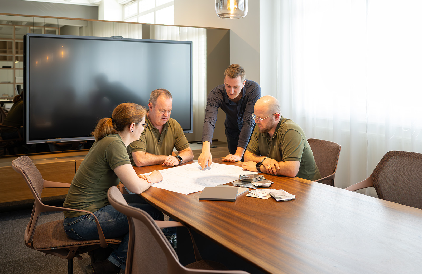 Projektteam bei einer Besprechung im modernen Konferenzraum mit Bauplänen auf dem Tisch.