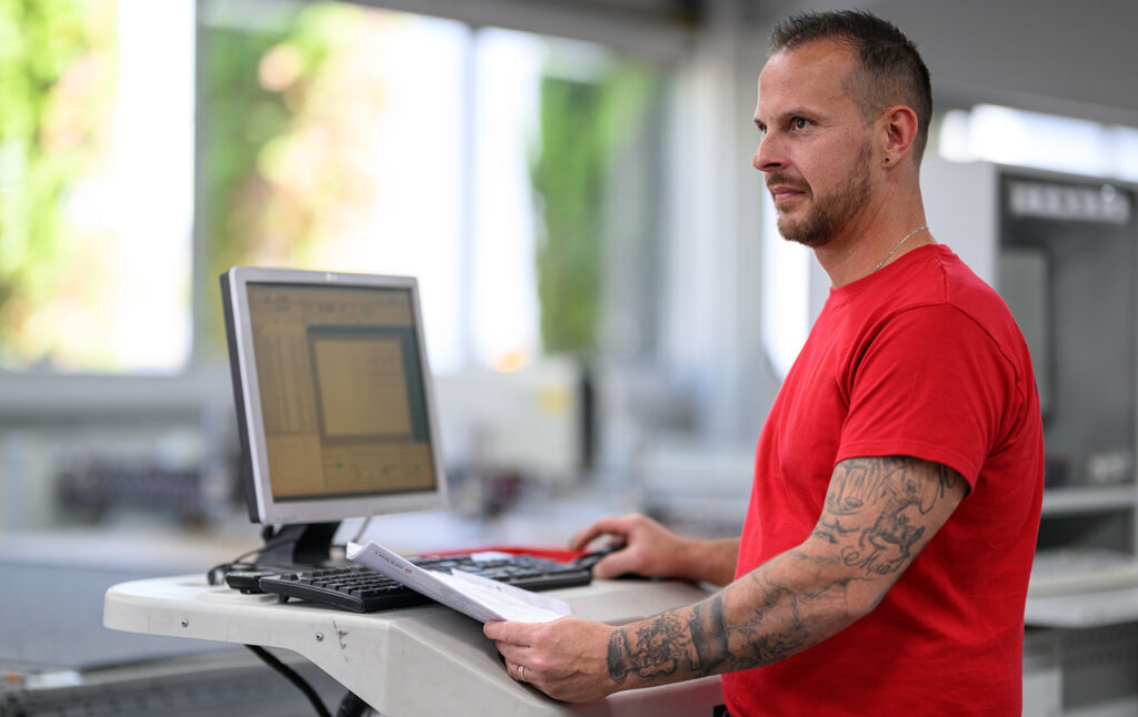 Maschinenbediener überwacht eine CNC-Anlage an einem Computerarbeitsplatz in der Produktion.