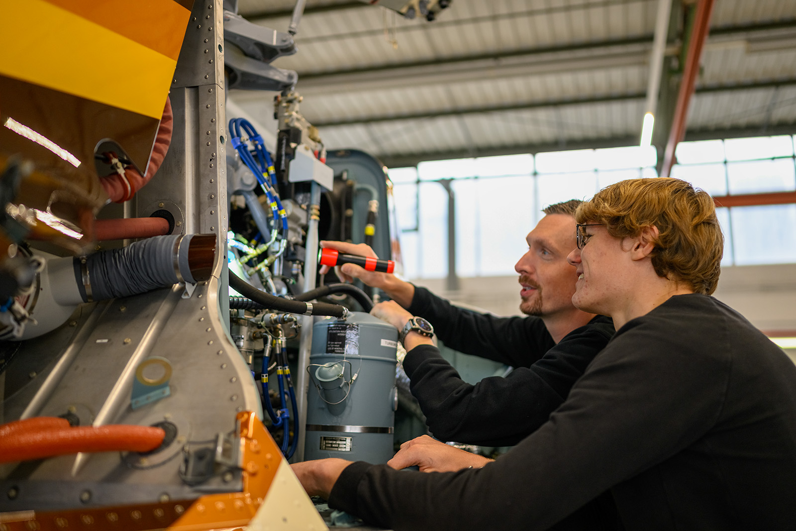 Techniker erklärt einem Auszubildenden die Wartung einer Industrieanlage.