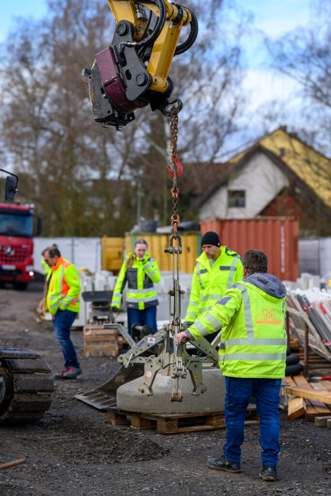 Zwei Mitarbeiter führen ein Betonfertigteil beim Kraneinheben