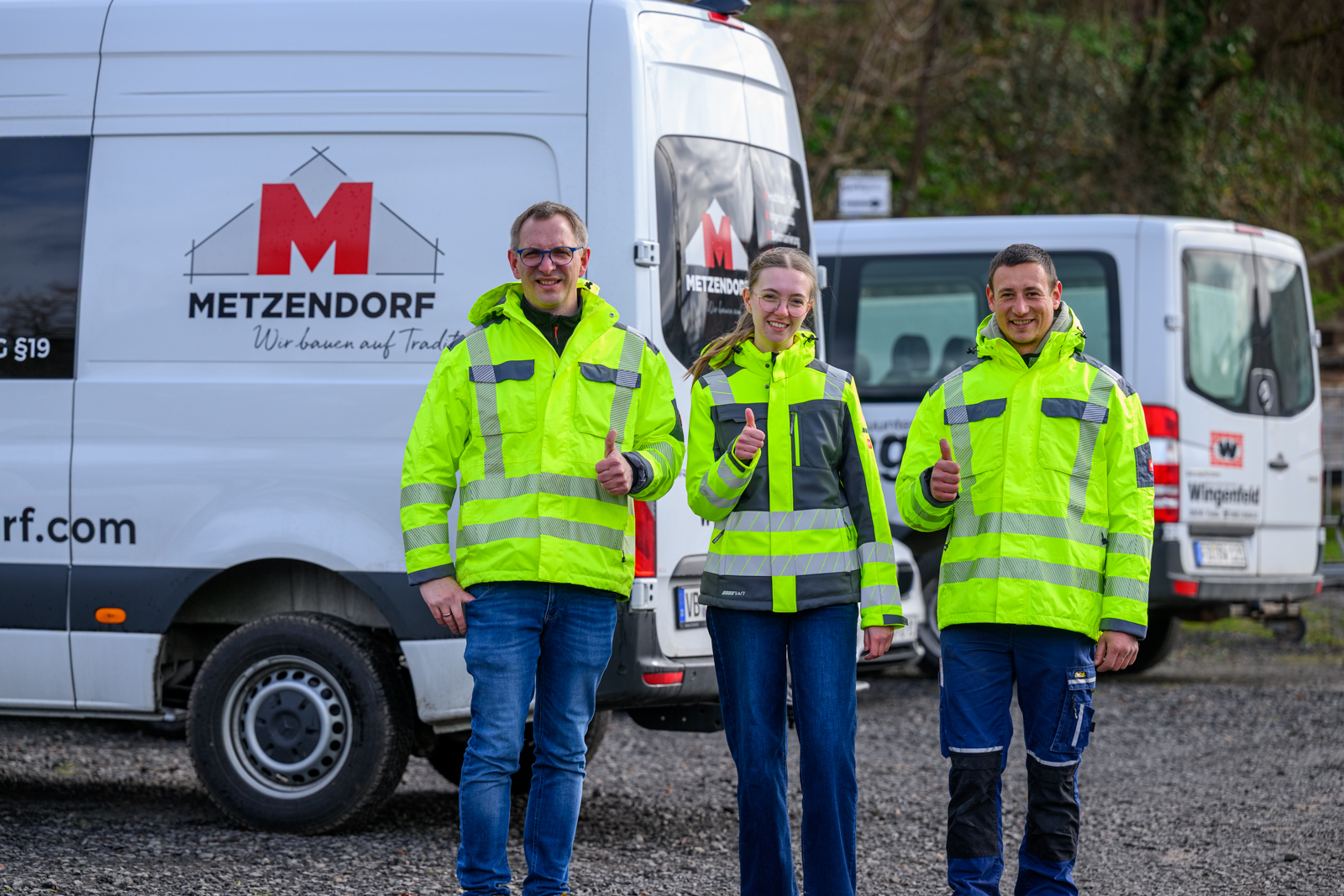 Drei Mitarbeiter stehen lächelnd vor firmeneigenen Transportern