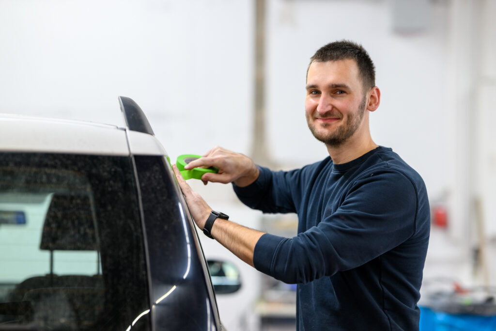 Lächelnder Mitarbeiter montiert Fensterleiste am Auto