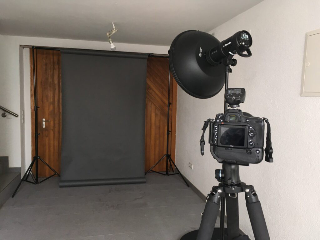 Kamera mit Teleobjektiv auf Stativ, Beauty Dish am Galgen, grauer Hintergrund zwischen zwei Türen