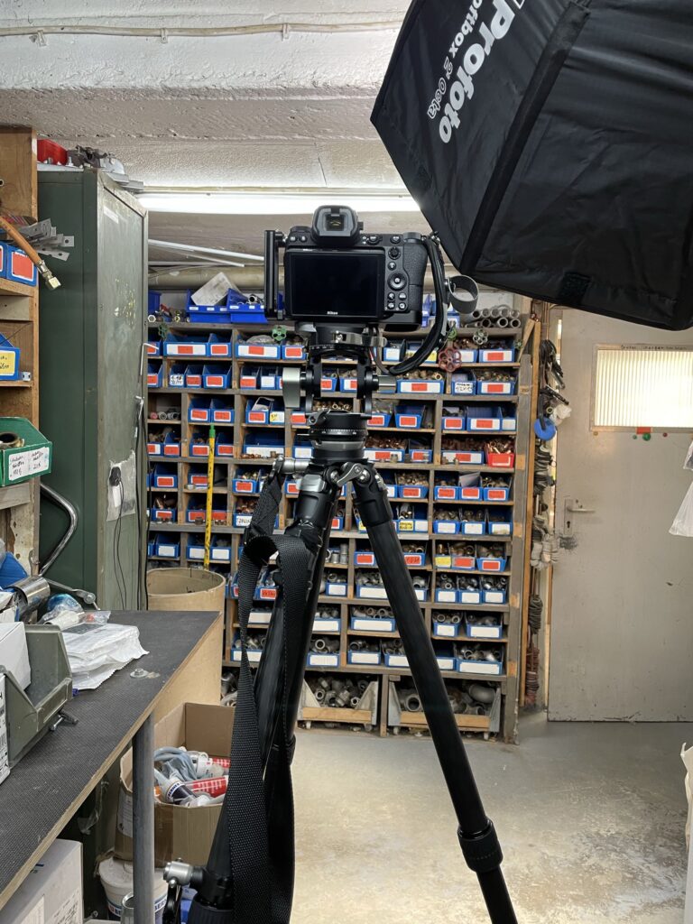 Kamera auf Stativ und Profoto-Softbox vor einem Regal mit Ersatzteilen in einer Werkstatt