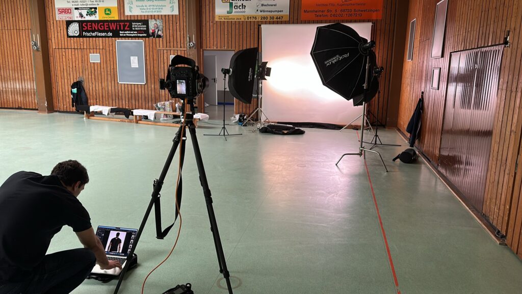 Mobiles Fotostudio mit hellem Hintergrund und Softboxen in einer Sporthalle, Laptop am Boden