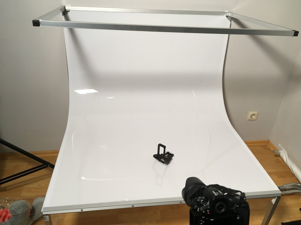Weißer Aufnahmetisch mit Hohlkehle, darauf ein kleines Produkt, Kamera im Vordergrund