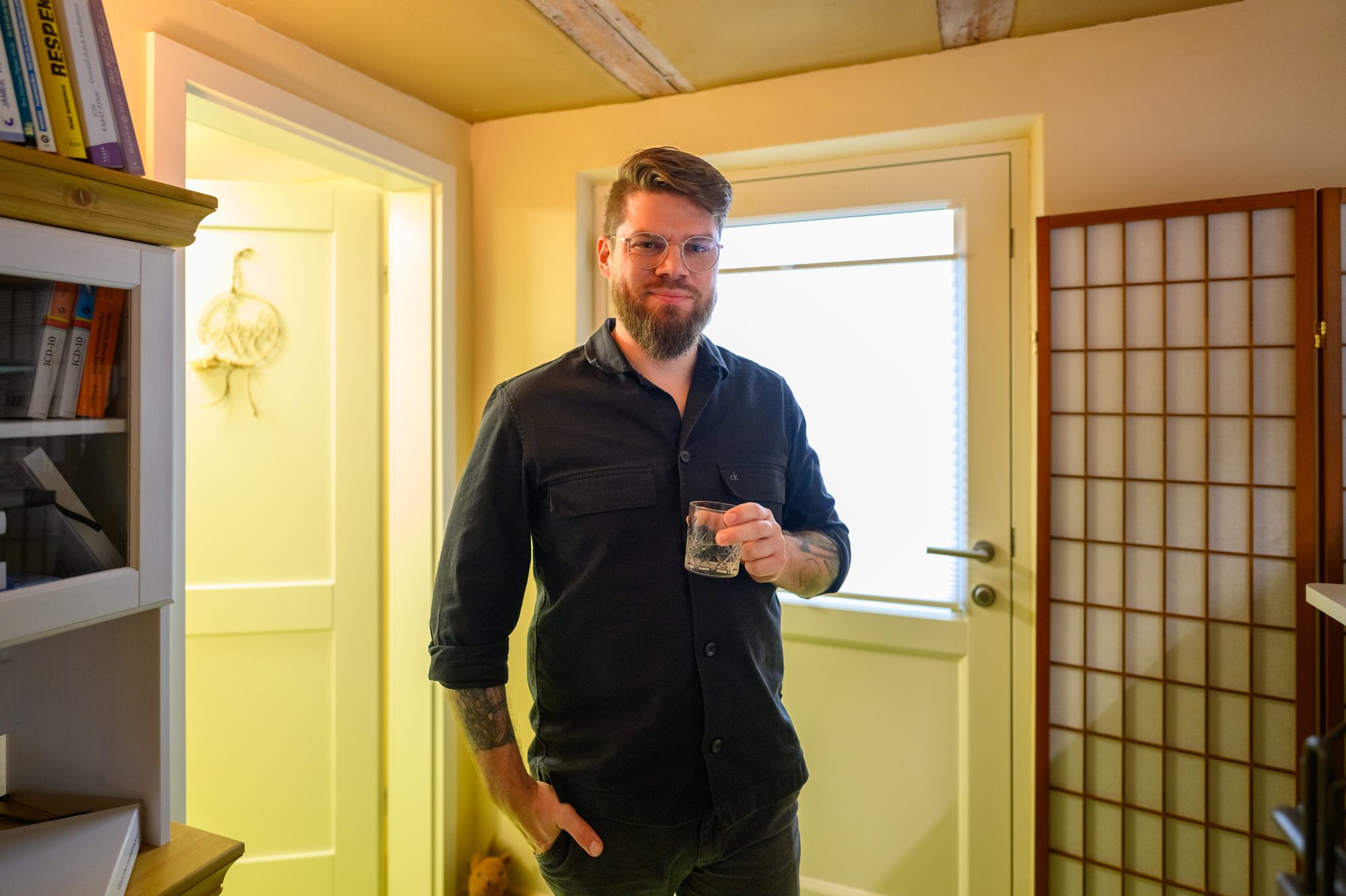 Ronny Mosebach steht mit einem Glas Wasser im hellen Flur seiner Praxis